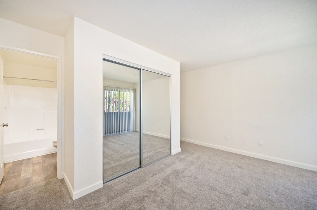 the living room and dining room of an apartment with mirrored doors and carpeting