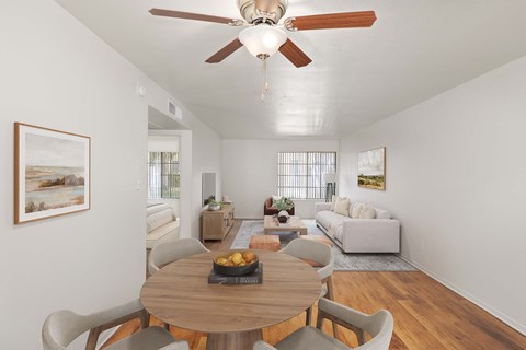 Dining room with wood-style vinyl plank flooring and ceiling fan with view to living room with large window.