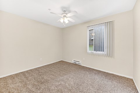 Apartment bedroom with carpet, window, and ceiling fan.