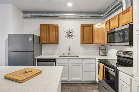 A kitchen with a black refrigerator, white cabinets, and a wooden cutting board on the counter.