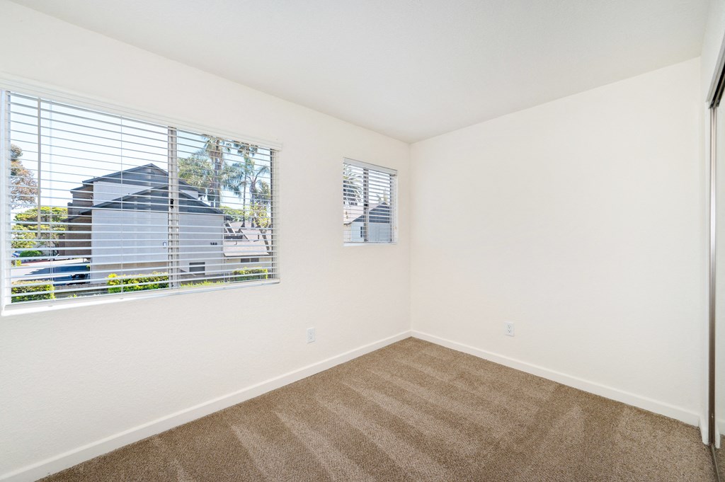 an empty bedroom with a large window and carpeted flooring