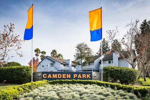 Camden Park monument sign with two flags over a gorgeous planter and the blue property exterior in the background.
