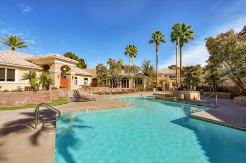 A large swimming pool in front of a house with palm trees.