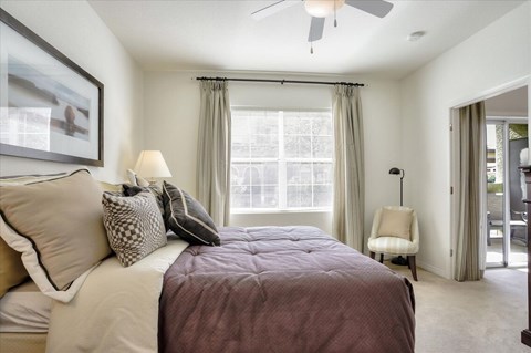 Carpeted bedroom with ceiling fan and window with lots of natural light.