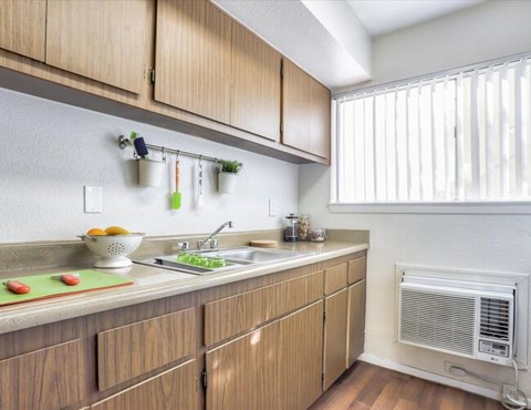 A kitchen with wooden cabinets and a window with blinds.