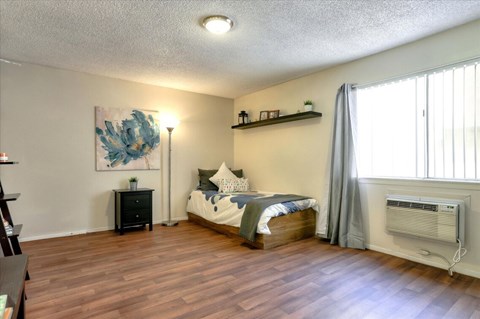 Private bedroom with wood-style vinyl plank flooring, window, and wall unit air conditioning.