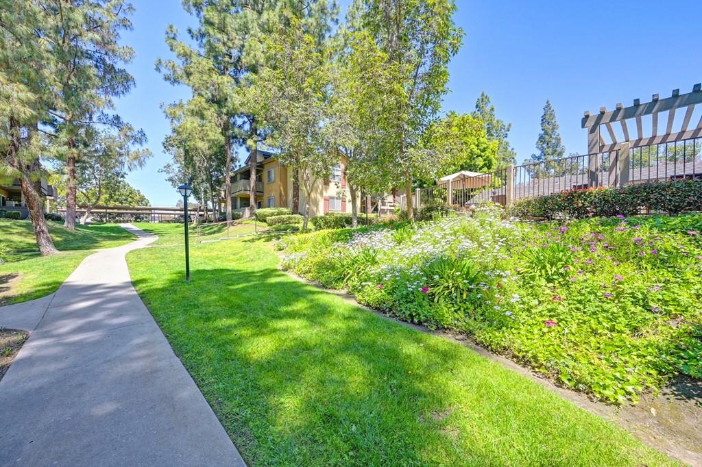 a sidewalk running through a park with trees and flowers