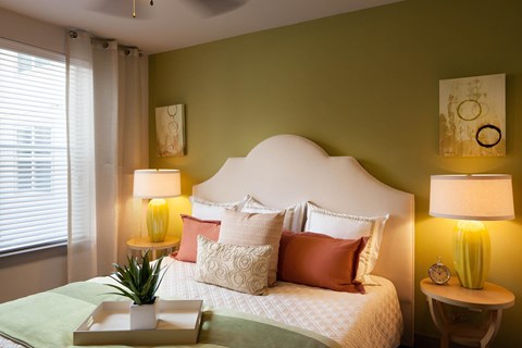 A bedroom with a bed, two lamps, and a plant.