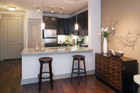 two bar stools in front of a kitchen counter with hanging lights and a stainless steel fridge in the background