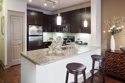 A kitchen with a granite countertop and dark brown cabinets and bar stools.
