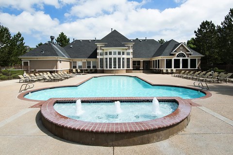 an apartment clubhouse behind a pool and fountain