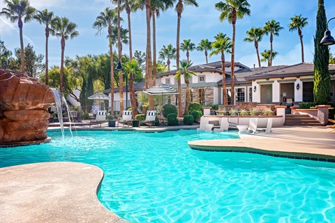 A large swimming pool surrounded by palm trees and a resident clubhouse.