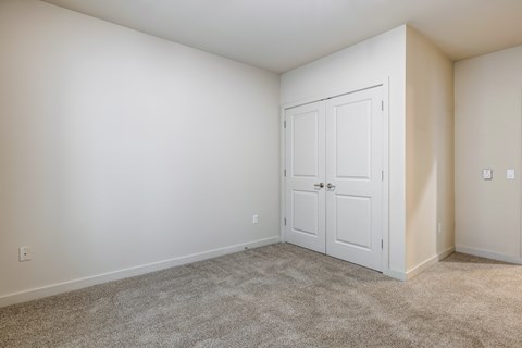 A white door is in the corner of a room with carpeted floor.