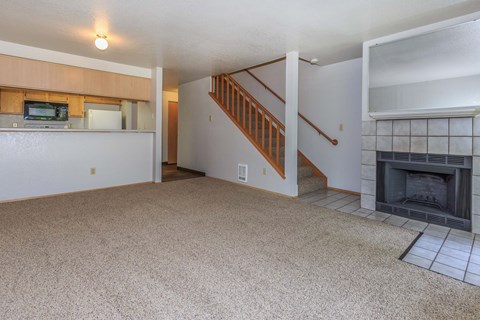 Living room with fireplace, stairs to second level, and view of kitchen with breakfast bar.