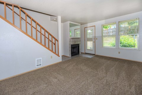 Carpeted living room with fireplace and staircase to second floor.