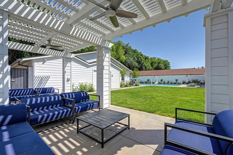 A patio with a white pergola and blue cushioned chairs.