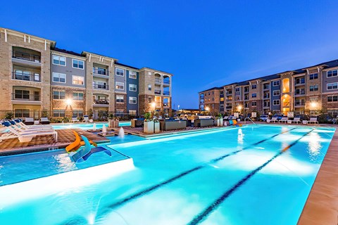 A large swimming pool in front of an apartment complex at night