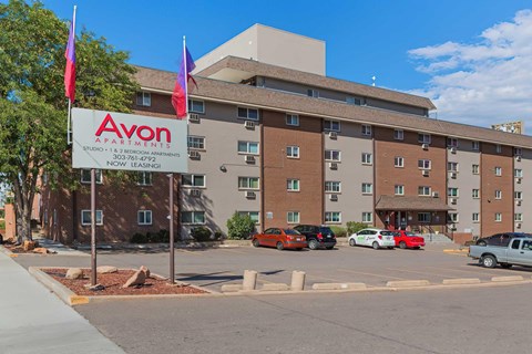 A parking lot in front of a multi-story apartment building with a sign that says Avon Apartments.