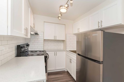 A kitchen with white cabinets and a stainless steel refrigerator and a black stove.