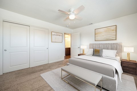 A bedroom with a bed, a bench, and a ceiling fan.