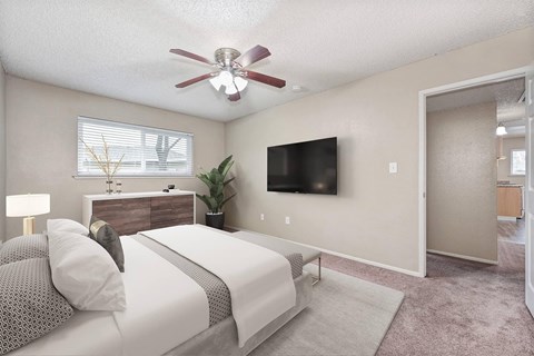 A bedroom with a bed, a dresser, a ceiling fan, and a flat-screen TV mounted on the wall.