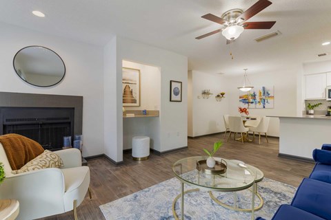 A modern living room with a fireplace, a glass coffee table, ceiling fan, and a blue sofa.