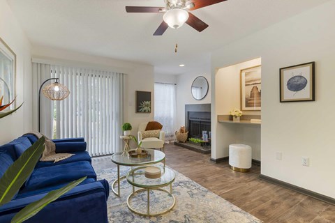 A living room with a blue couch and a glass coffee table and ceiling fan overhead.