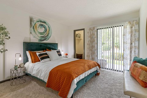 A bedroom with a large bed and a painting on the wall and sliding glass doors in the back.
