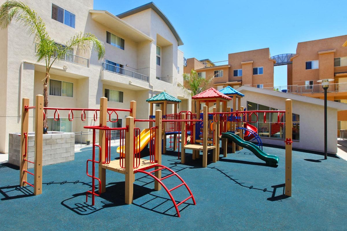 Community playground with light gray and tan building exterior in background.