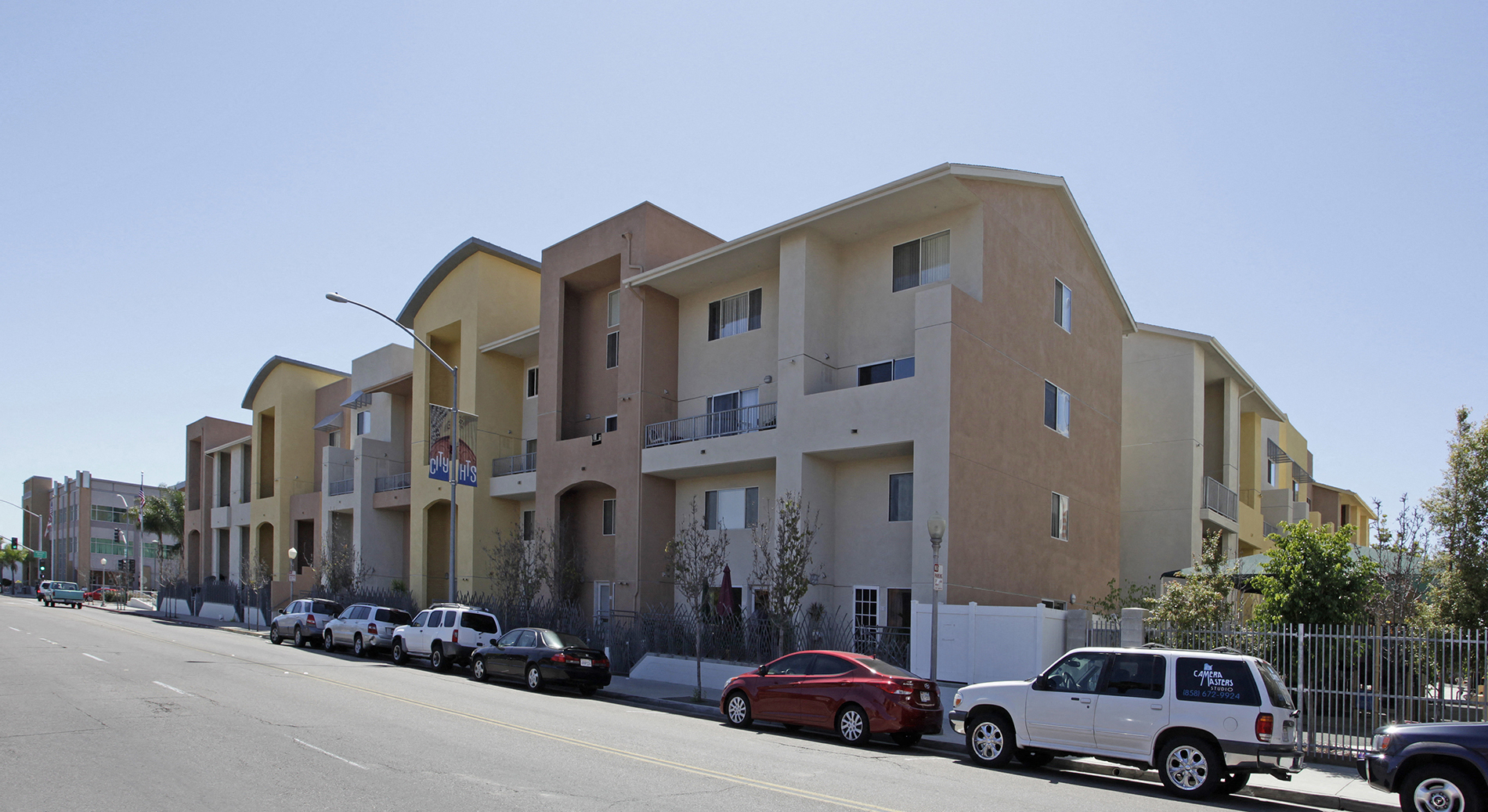 A row of apartment buildings with cars parked in front.