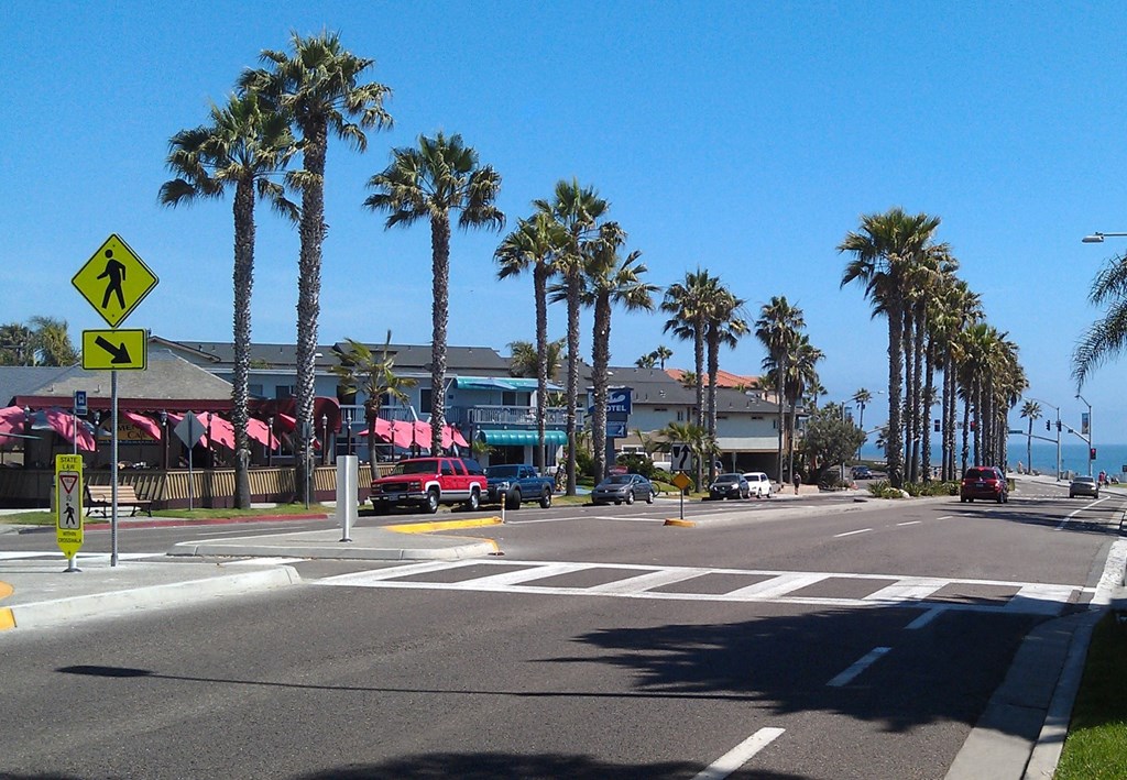 a city street with palm trees and a beach in the background