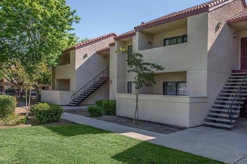The exterior of the apartment building with grass areas and trees.