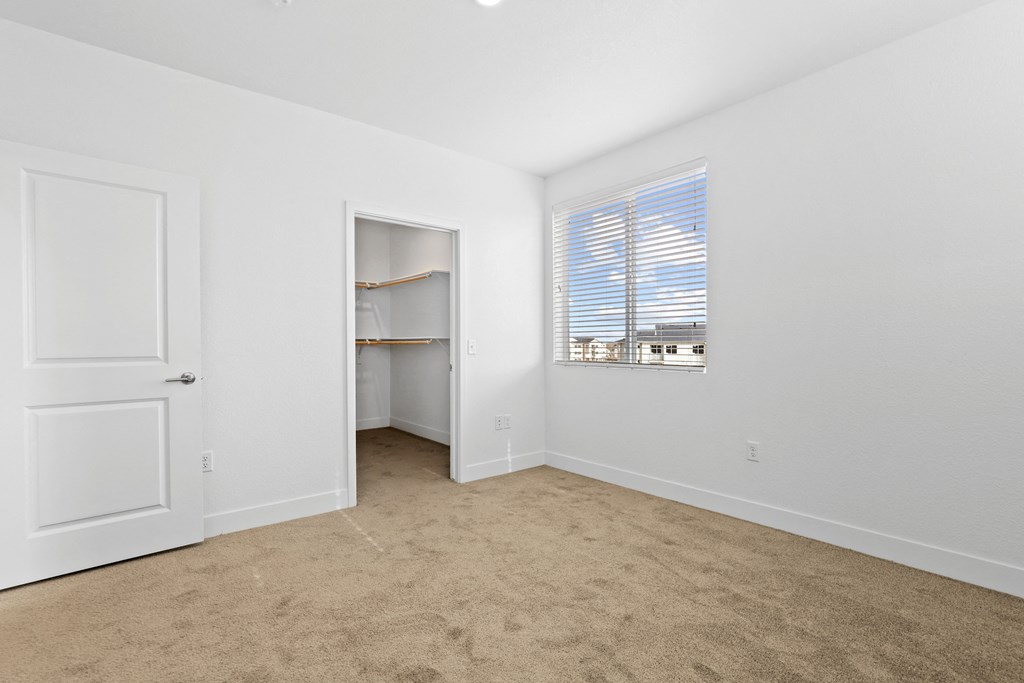 a bedroom with white walls and carpet and a door to a closet