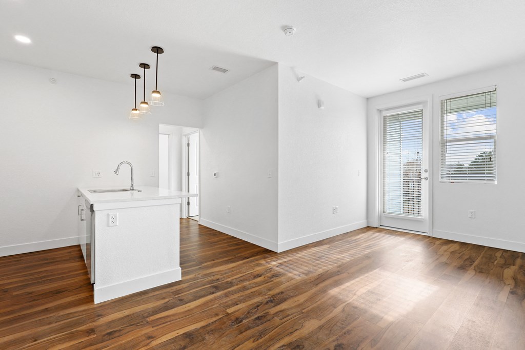 a living room with white walls and a kitchen with wood flooring