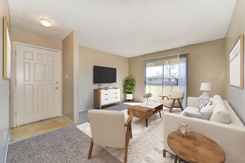 A living room with carpet, a couch, 2 chairs, a rug, and a coffee table. In the background you can see a sliding glass door that leads to a balcony.
