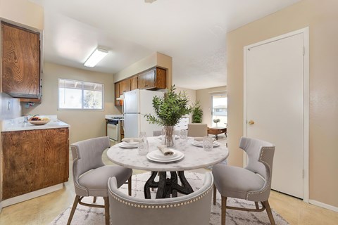 A dining room with a table set and the kitchen in the near background.