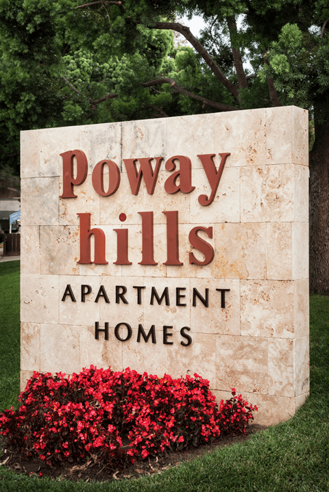 A stone sign for Poway Hills Apartment Homes with red flowers in front.
