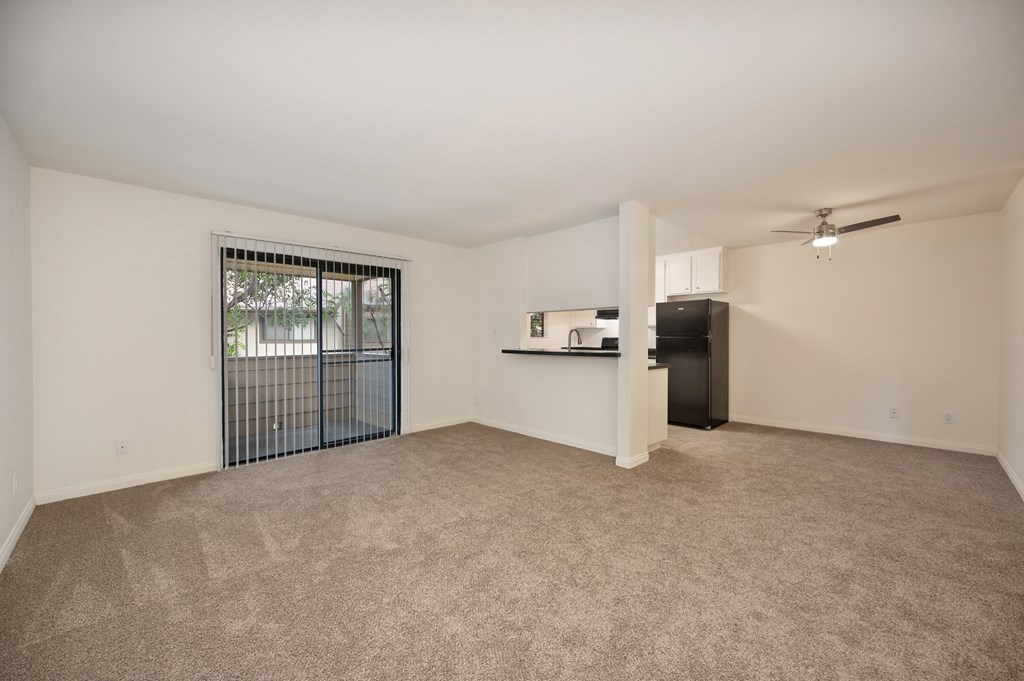 the living room and kitchen of an apartment with a large door to a balcony
