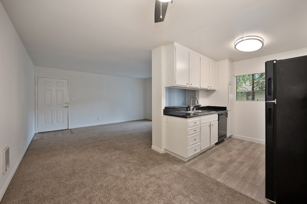 an empty kitchen and living room with white cabinets and a black refrigerator