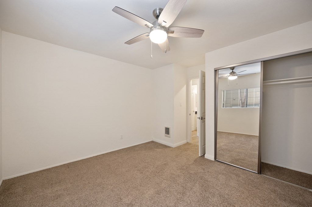 an empty living room with a ceiling fan and a mirrored closet