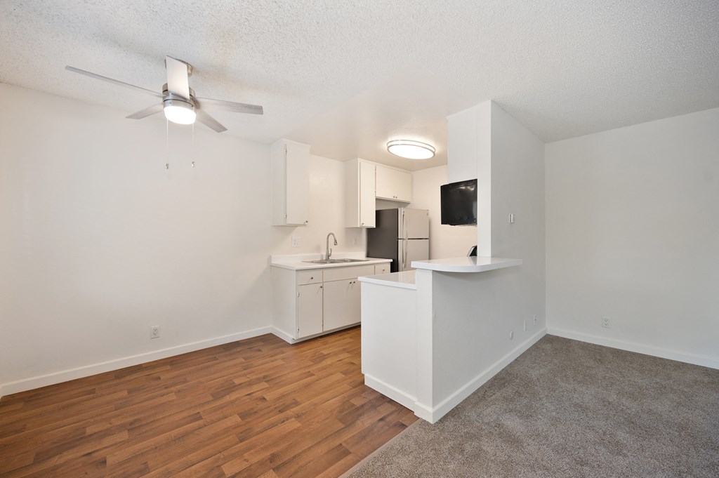 an empty living room and kitchen with wood flooring and a ceiling fan