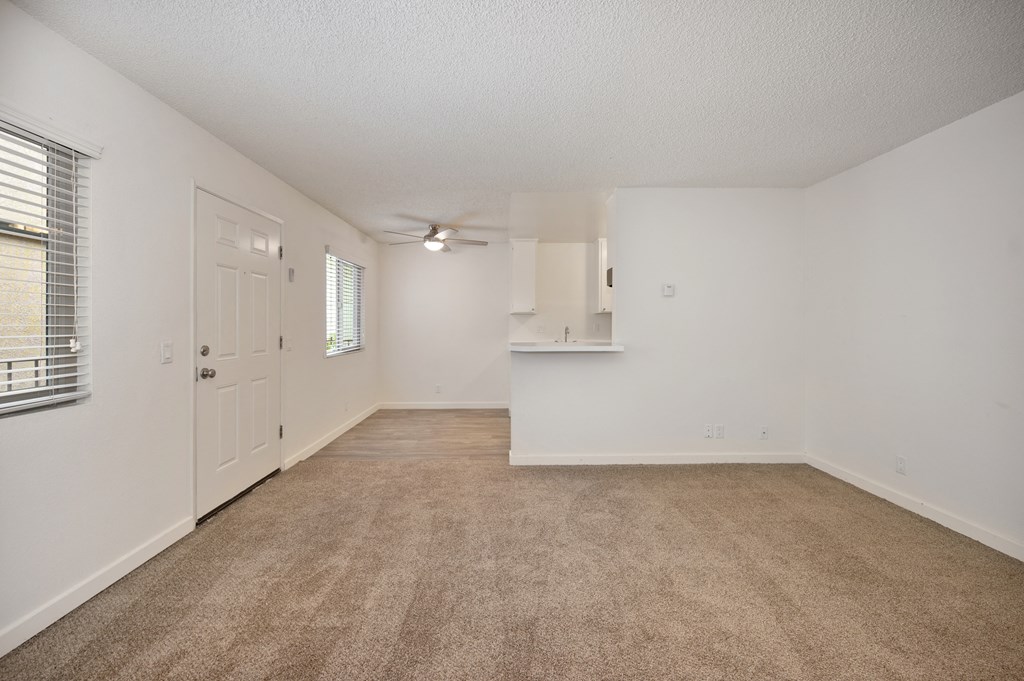 a spacious living room with carpet and a door to a kitchen
