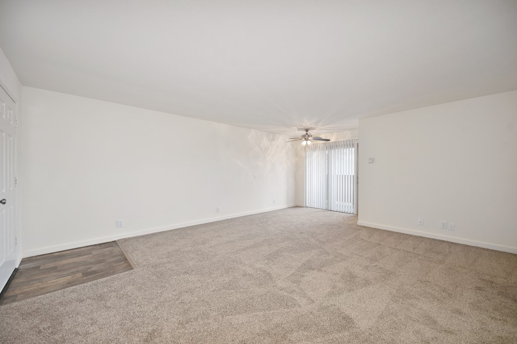 a living room with carpet and white walls and a ceiling fan