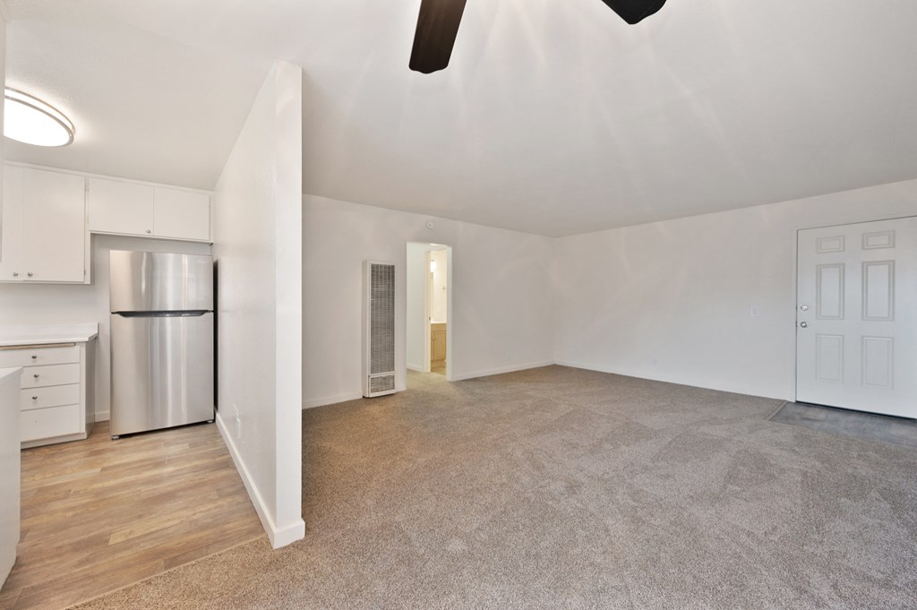 an empty living room with white walls and a stainless steel refrigerator