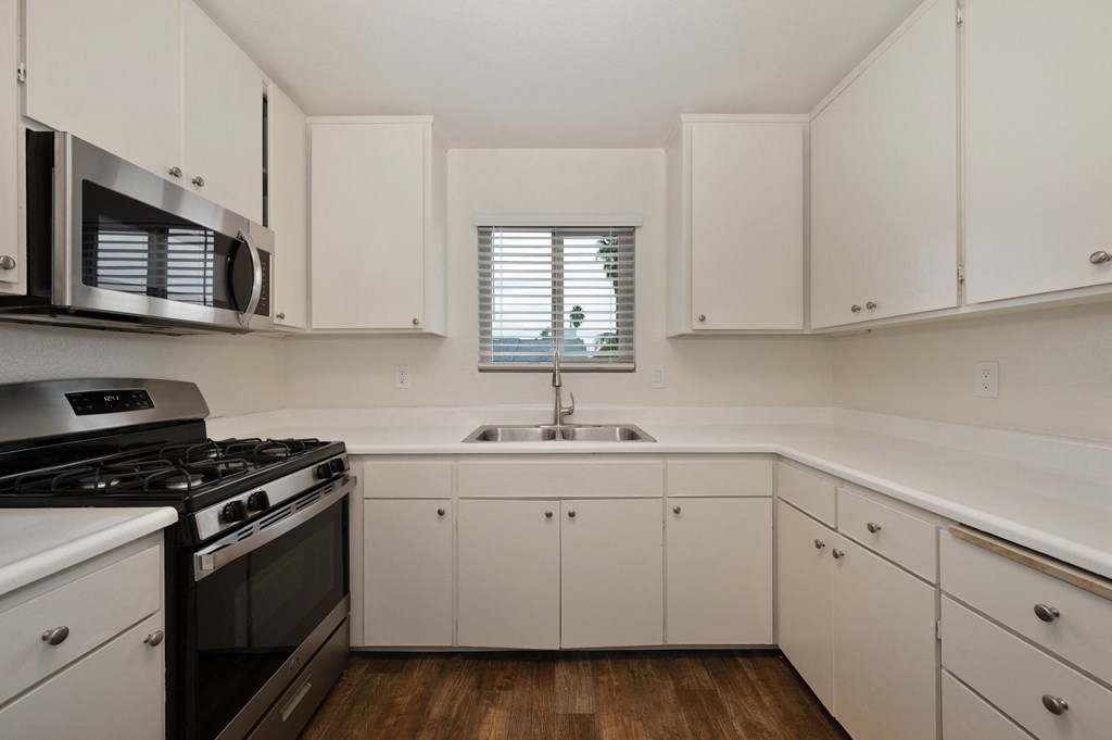 an empty kitchen with white cabinets and stainless steel appliances and a window