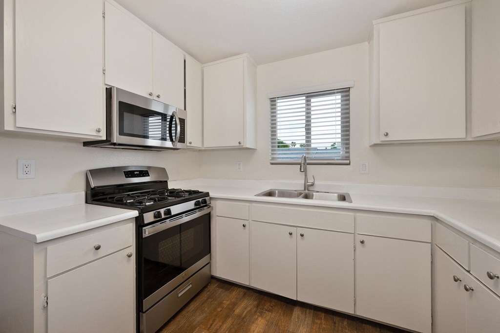 an empty kitchen with white cabinets and stainless steel appliances and a window