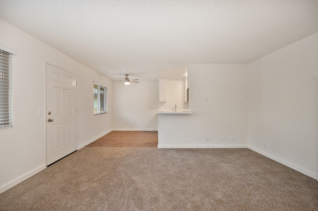 an empty living room and kitchen with white walls and carpet