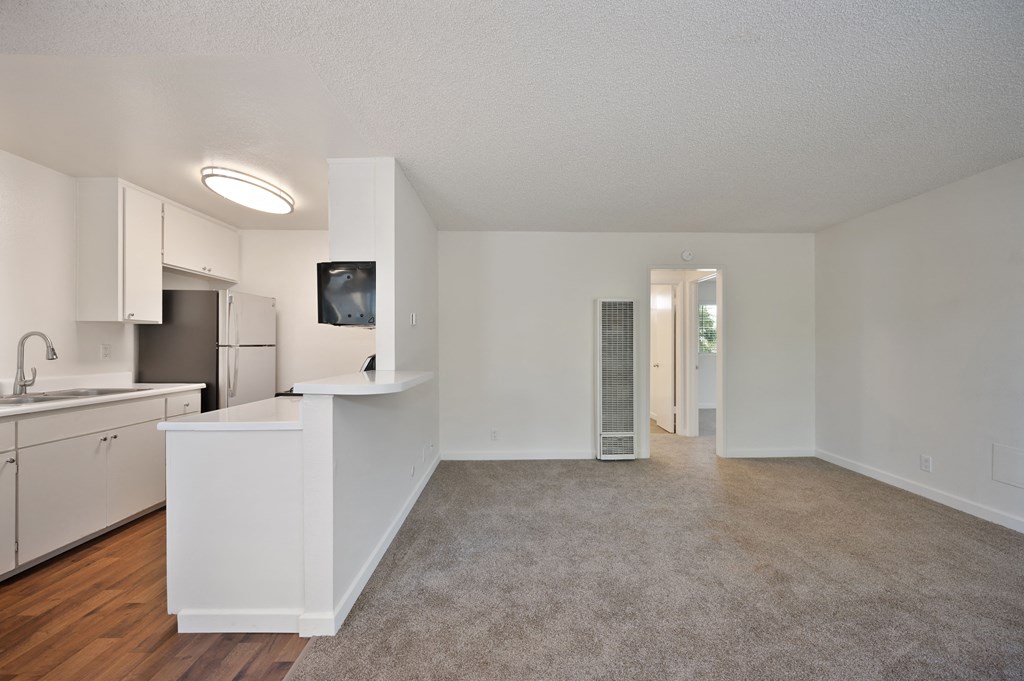 the living room and kitchen of an apartment with white walls and wood flooring