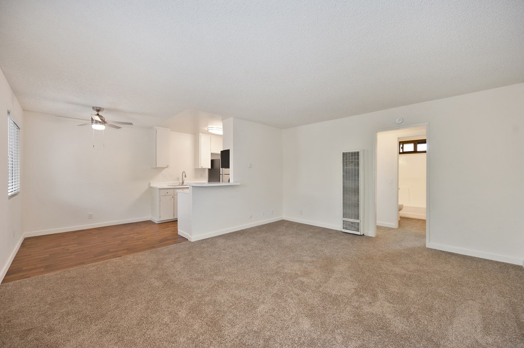 an empty living room with a kitchen and a ceiling fan