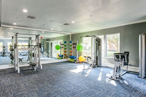 A spacious gym with various exercise equipment and a large mirror on the wall.